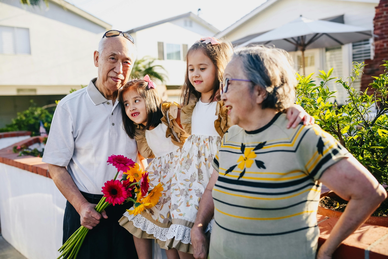 Alltagsengel plus - Alltagshelfer - Dieses Bild zeigt ein älteres Ehepaar mit einem Strauß bunter Blumen und zwei kleinen Kindern in einer sonnigen Umgebung im Freien.